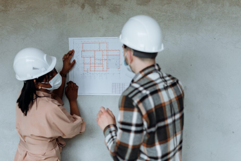 Tradesman and tradewoman in white hard hats looking at site map